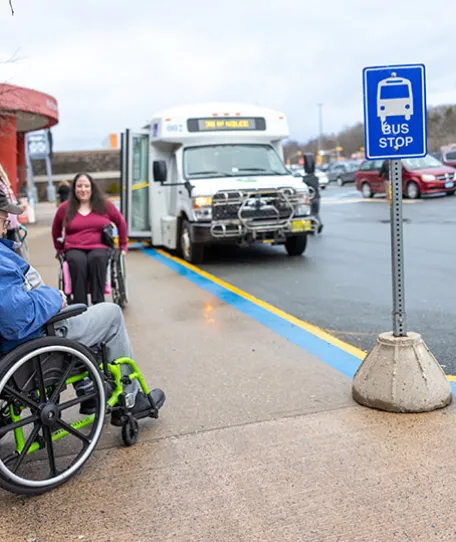 Two people in wheelchairs at bus stop