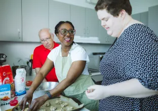 Three people standing in a kitchen baking cookies.